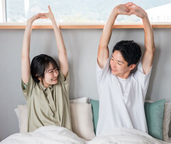 couple stretching in bed after night of good sleep